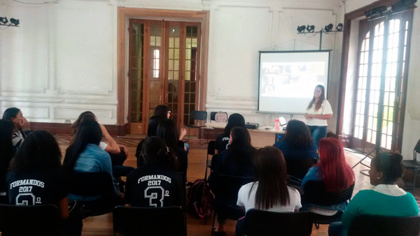 Priscyla com tela de projeção às suas costas, palestra para diversos alunos